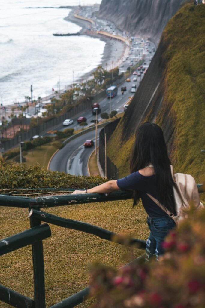 Mujer contemplando la vista del Malecón de Miraflores con vía costera y acantilados sobre el Pacífico