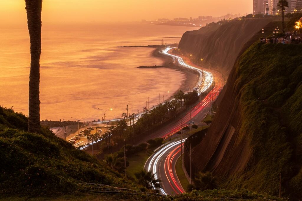Atardecer sobre la costa de Lima con luces de tráfico bordeando el Pacífico, frente a Barranco, distrito bohemio de lujo.