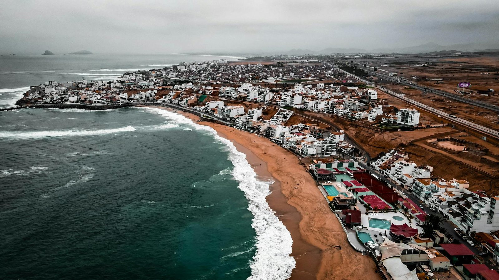 Vista aérea de la costa de Lima frente al Pacífico, con cityscape urbano coherente con el frente marítimo de San Miguel.